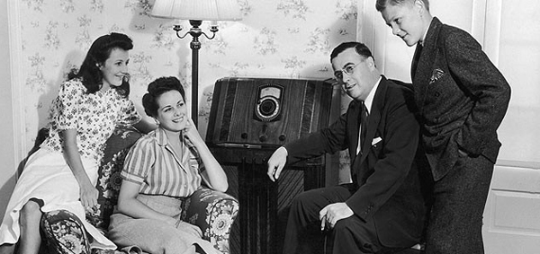 A family in the 1930s listens intentlyl to a large radio.